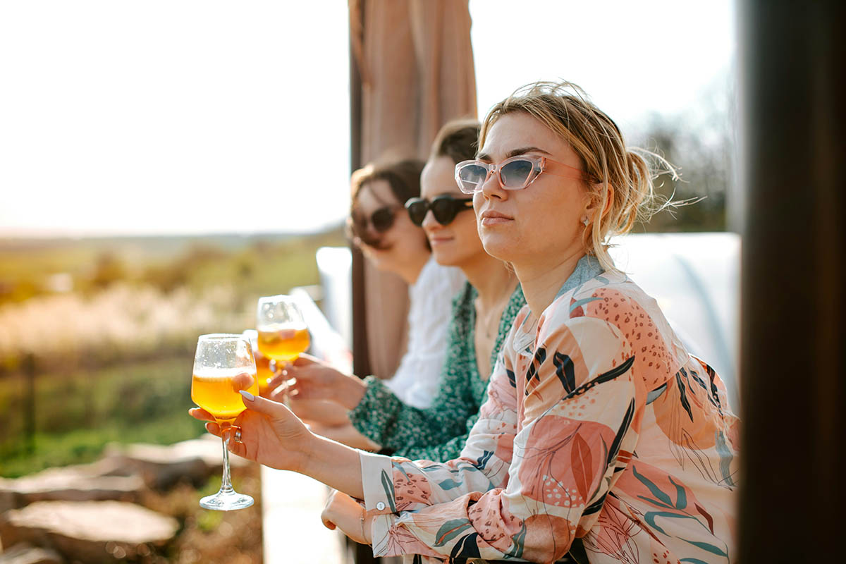 Friends looking over balcony railing and holding glasses of wine.